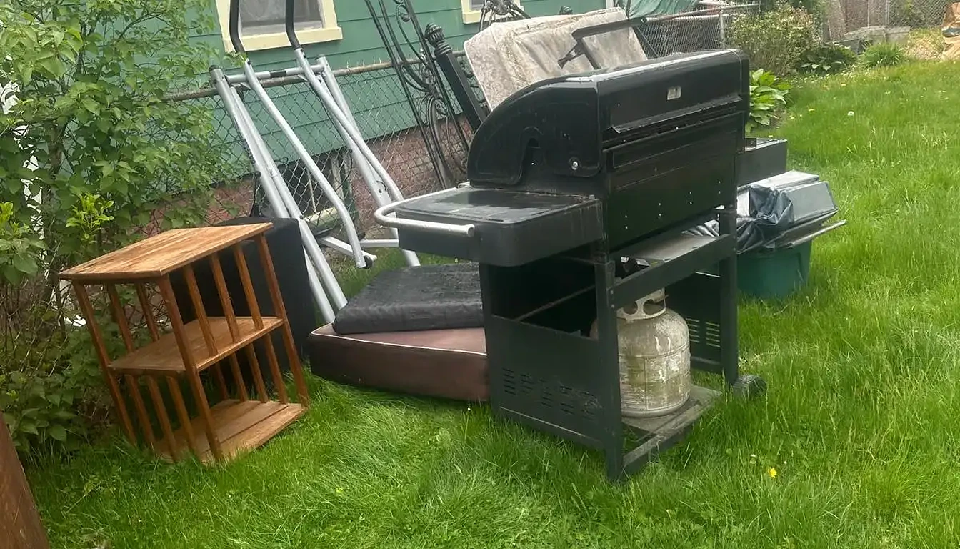 Old grill, exercise machine and furniture on a side lawn before removal