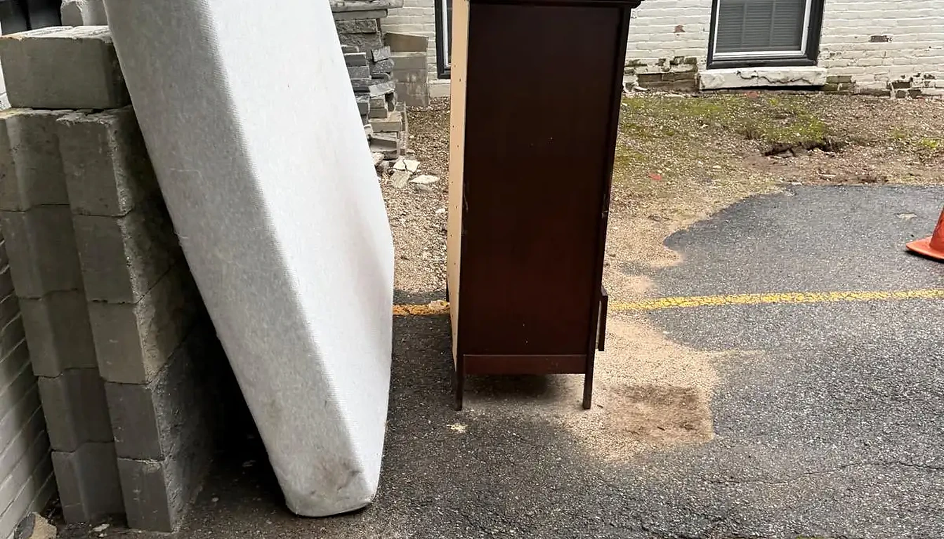 Mattress and dresser left beside a brick building before removal