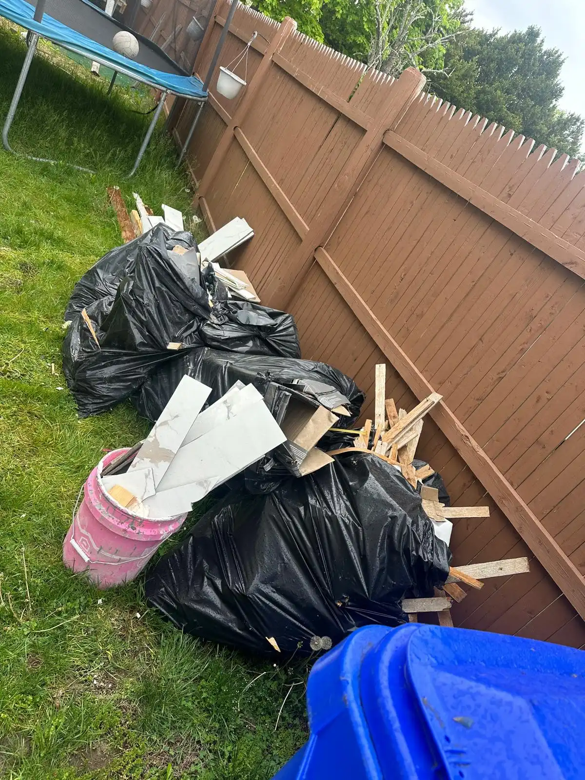 Bags of debris and scrap wood along a backyard fence before removal
