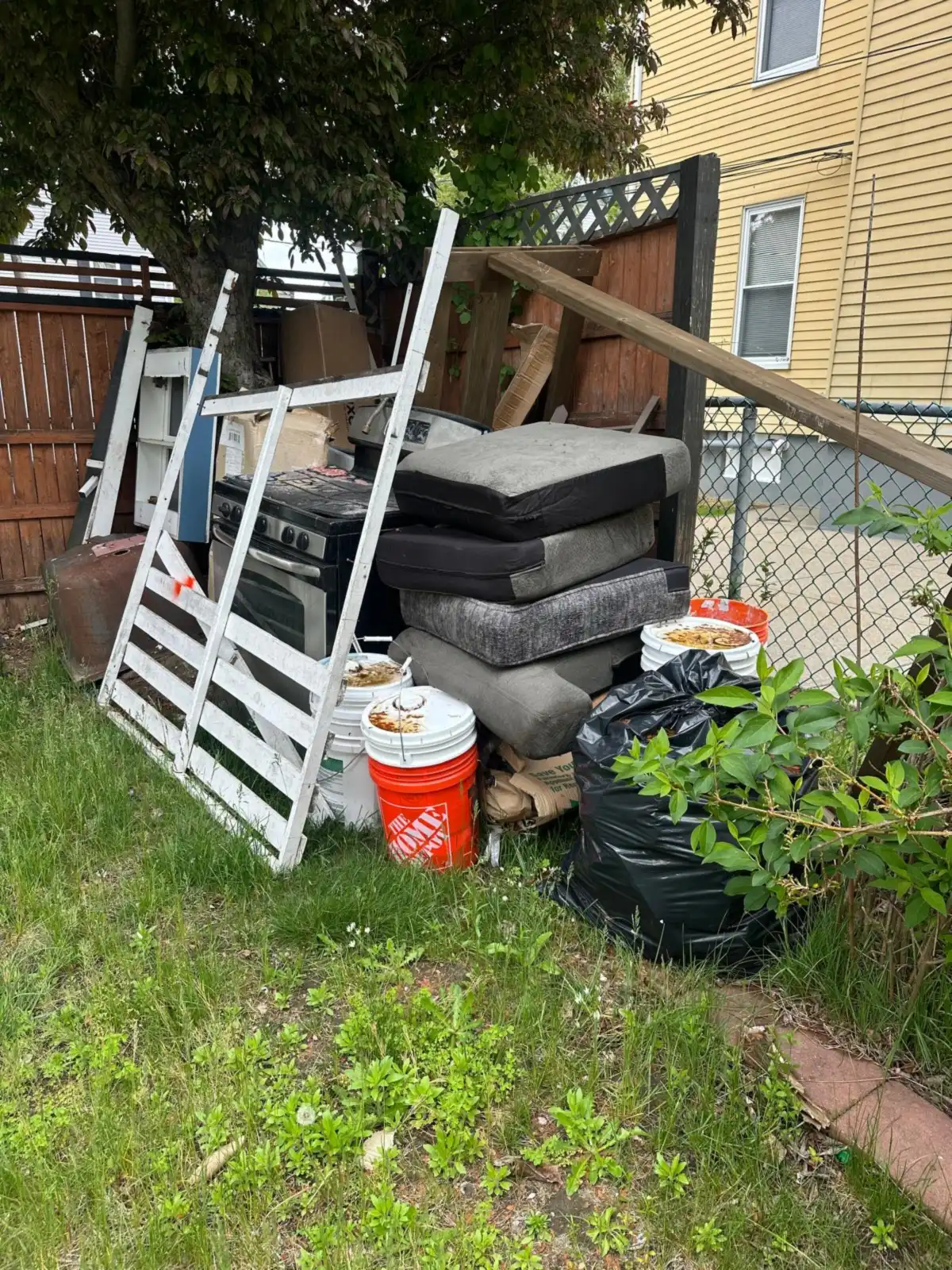 Cushions, bed frame and old furniture piled under a tree before removal
