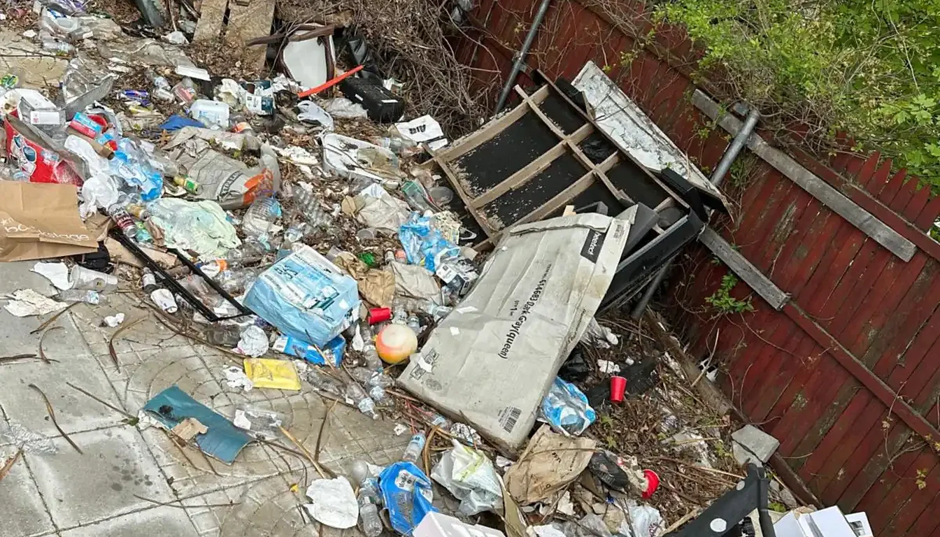 Fenced yard covered in trash and broken furniture before a cleanout