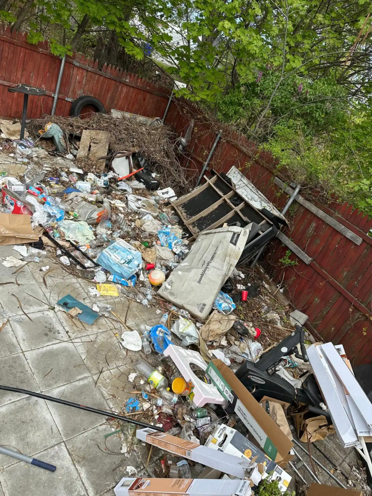 Fenced yard covered in trash and broken furniture before a cleanout