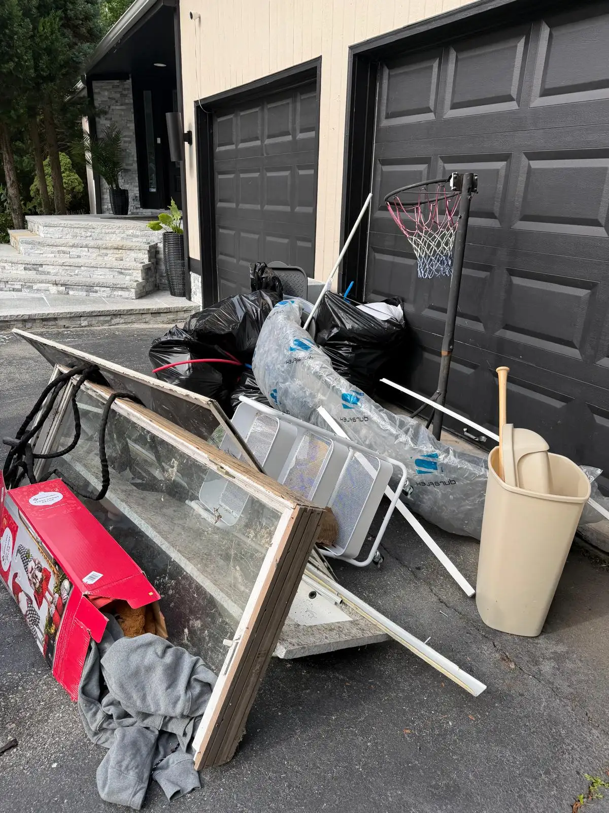 Window frame, bags and old items piled in front of a garage before removal