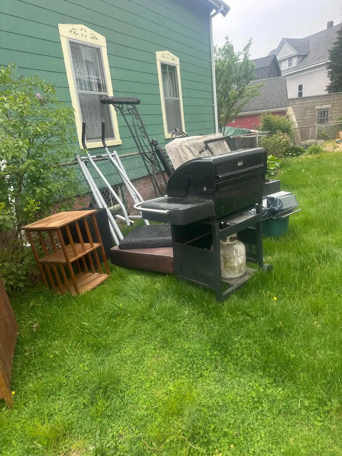 Old grill, exercise machine and furniture on a side lawn before removal