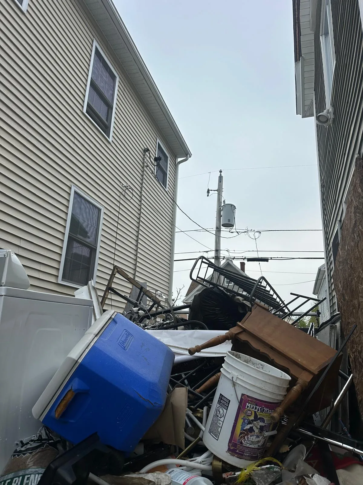 Cooler, buckets and scrap metal piled between two houses before cleanup