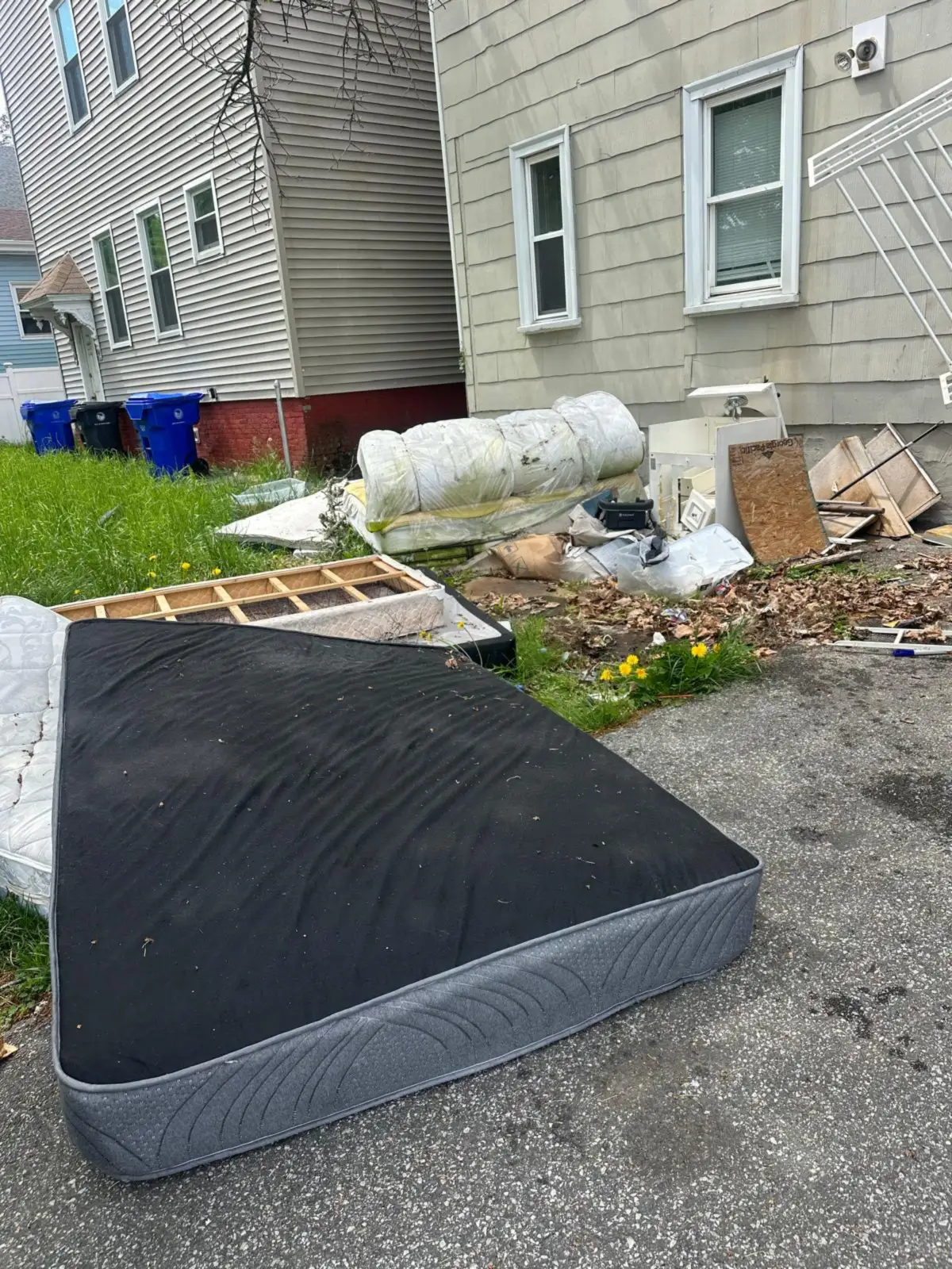 Mattress, box spring and debris beside a driveway before removal
