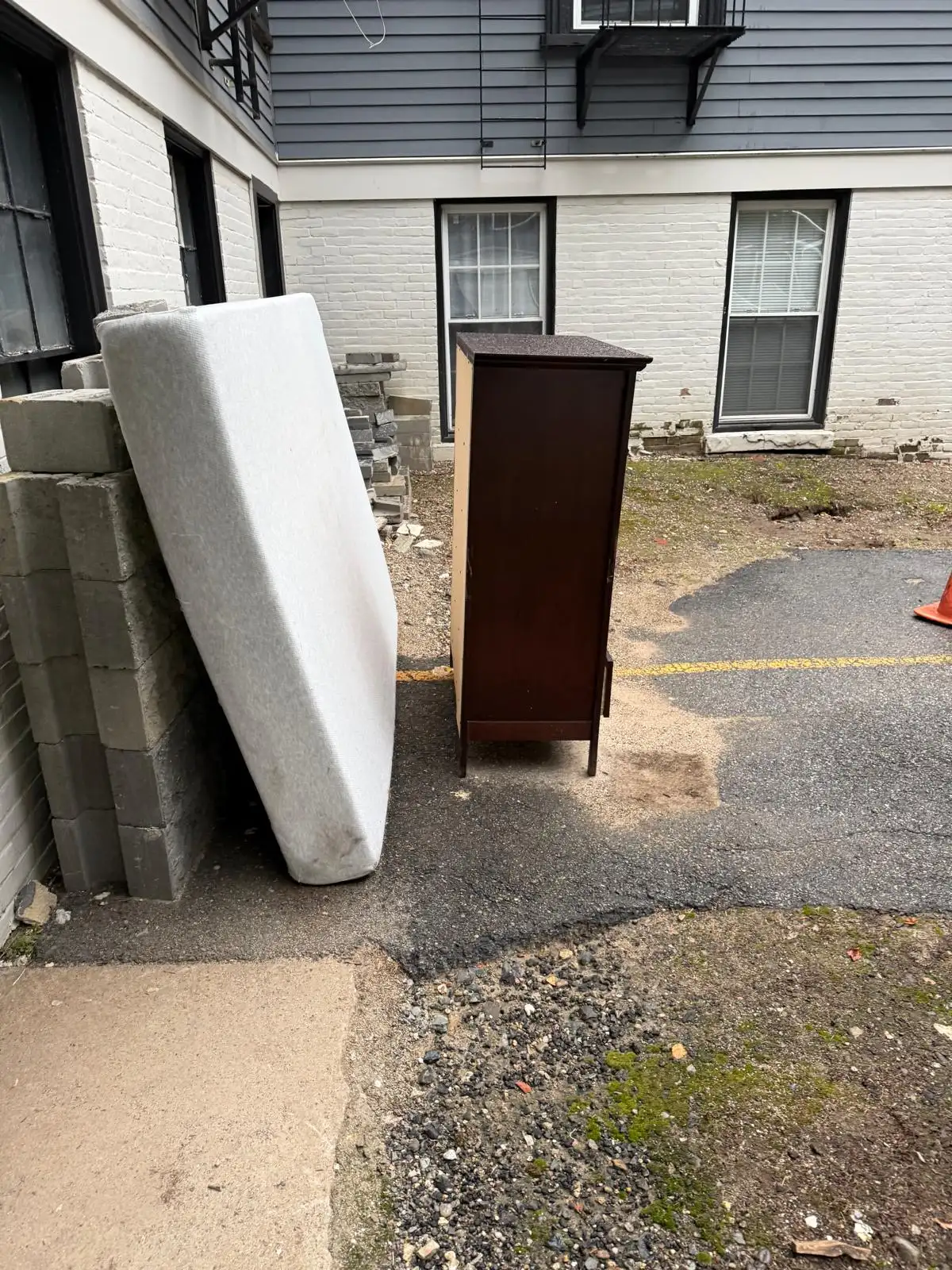 Mattress and dresser left beside a brick building before removal