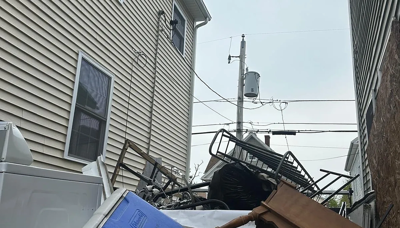 Cooler, buckets and scrap metal piled between two houses before cleanup