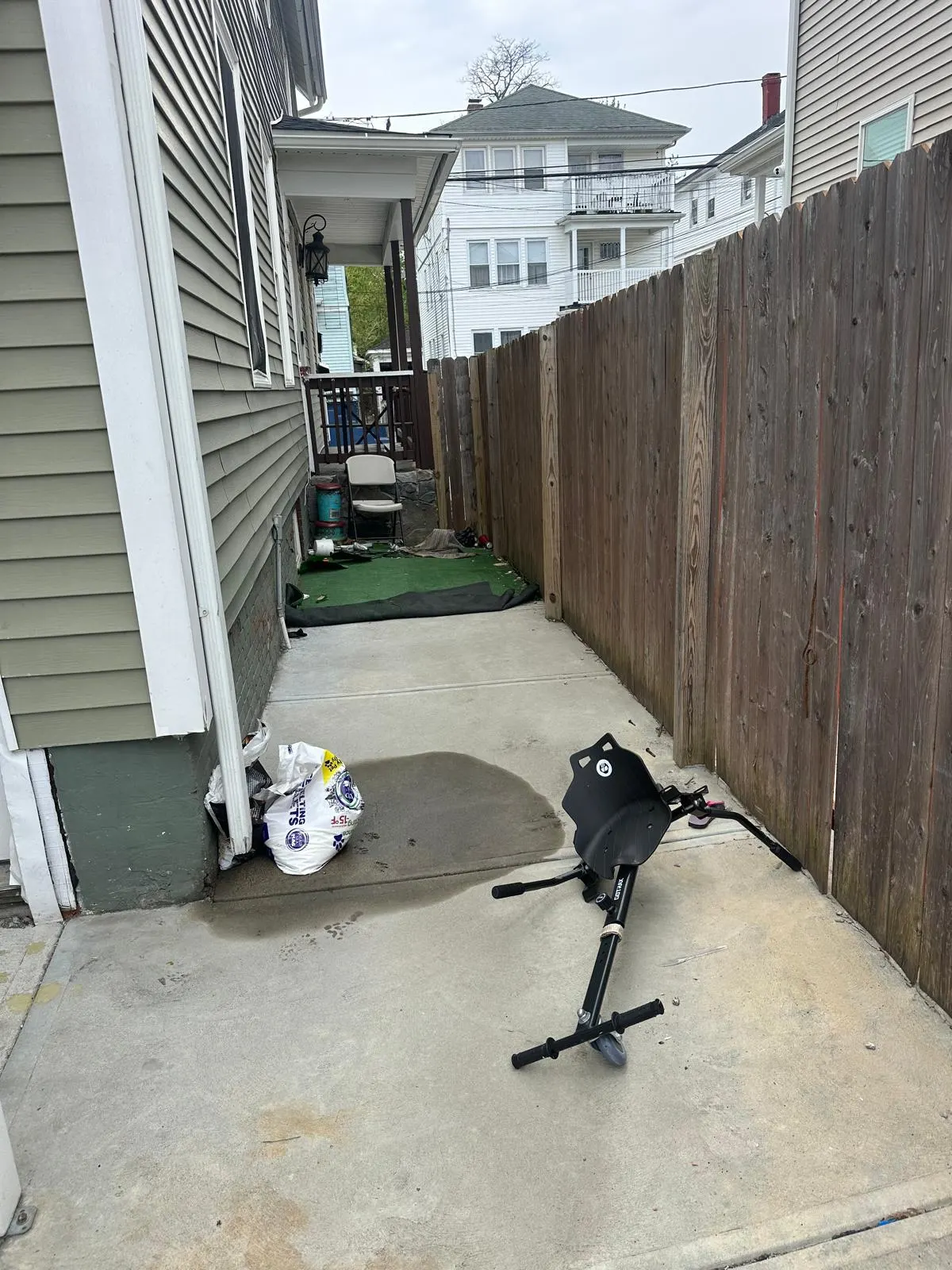 Scooter and bagged trash in a narrow side yard before junk removal